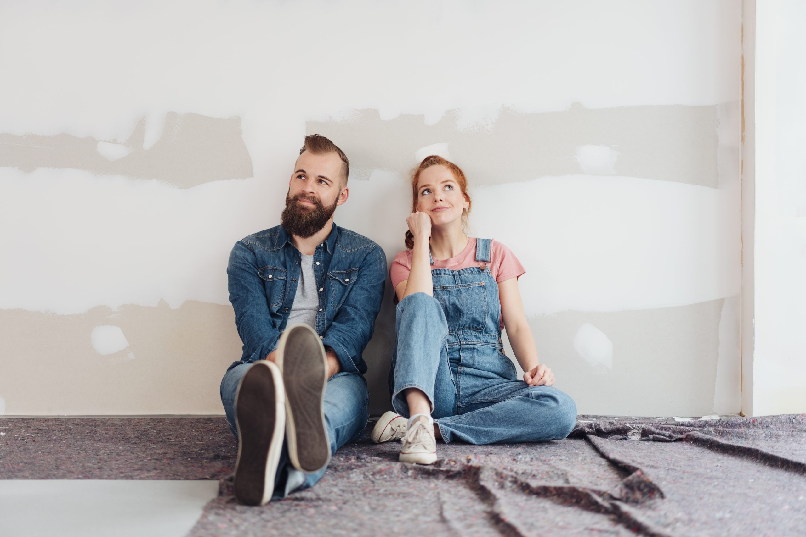 A young couple sitting on the floor side by side contemplating their handiwork during DIY renovations